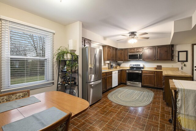kitchen featuring light countertops, dark brown cabinetry, a ceiling fan, appliances with stainless steel finishes, and brick floor