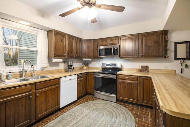 kitchen featuring butcher block countertops, brick patterned floor, a sink, a ceiling fan, and appliances with stainless steel finishes