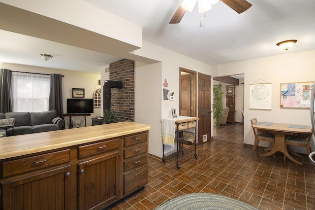 kitchen featuring a ceiling fan, a wood stove, wooden counters, open floor plan, and baseboards