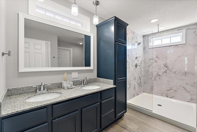 full bathroom featuring double vanity, a sink, a marble finish shower, and wood finished floors