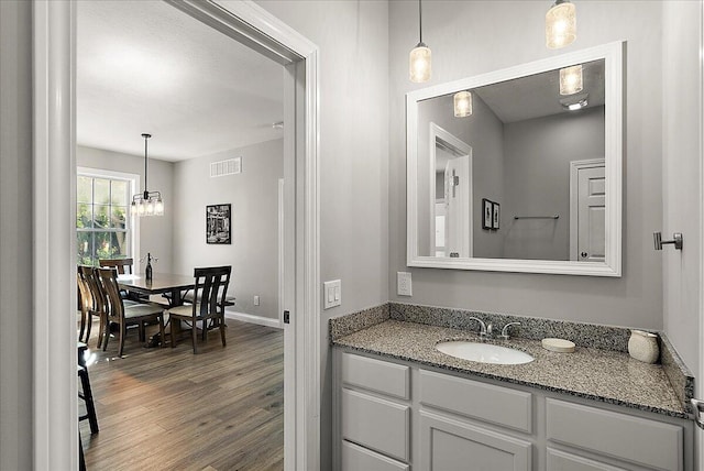 bathroom featuring visible vents, a chandelier, baseboards, wood finished floors, and vanity