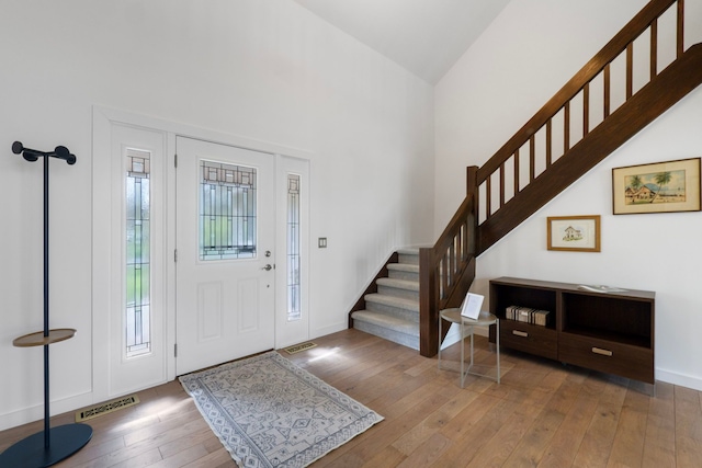 entrance foyer with wood-type flooring, visible vents, stairs, and a towering ceiling