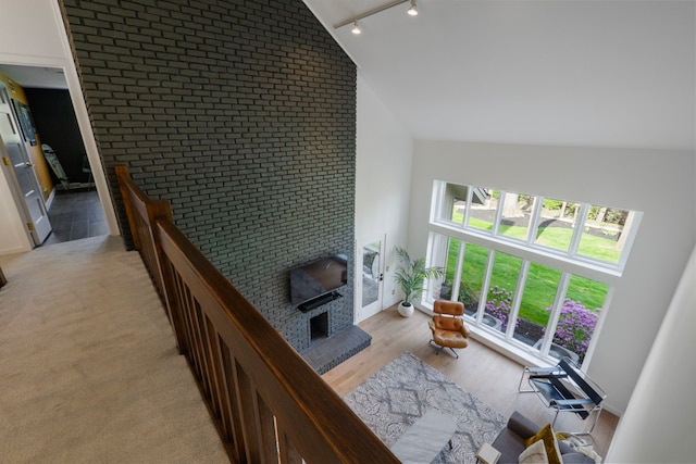 living room with brick wall, a fireplace, rail lighting, high vaulted ceiling, and light wood-style flooring