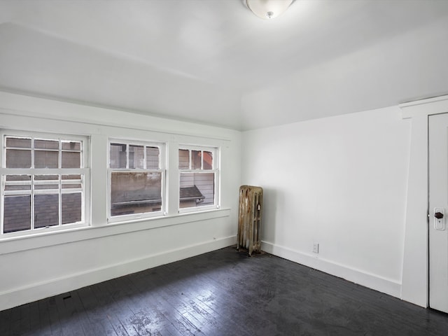 empty room featuring radiator heating unit, dark wood-style flooring, baseboards, and lofted ceiling