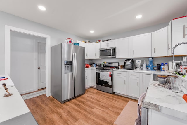 kitchen with light wood-style flooring, a sink, white cabinetry, light countertops, and appliances with stainless steel finishes