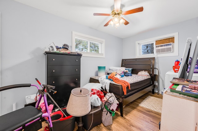 bedroom with a wall mounted AC, wood finished floors, and a ceiling fan