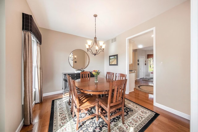 dining space featuring visible vents, baseboards, a chandelier, and wood finished floors