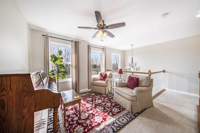 carpeted living area with ceiling fan with notable chandelier and baseboards