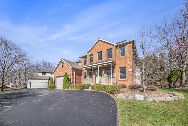 traditional home featuring brick siding, an attached garage, covered porch, and driveway