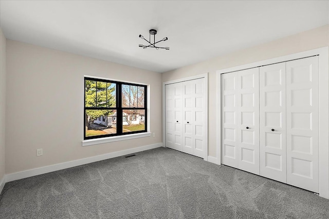 unfurnished bedroom featuring two closets, carpet flooring, baseboards, and an inviting chandelier
