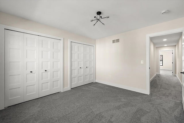 unfurnished bedroom featuring dark carpet, two closets, baseboards, and visible vents