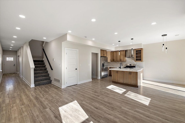 kitchen featuring visible vents, wall chimney range hood, light countertops, open floor plan, and appliances with stainless steel finishes