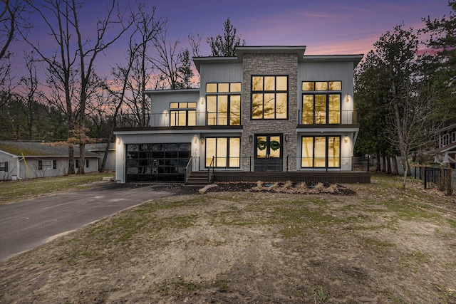 rear view of house with driveway, stone siding, and a balcony