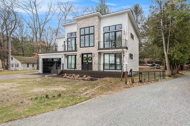 modern home featuring fence, stone siding, a balcony, an attached garage, and driveway