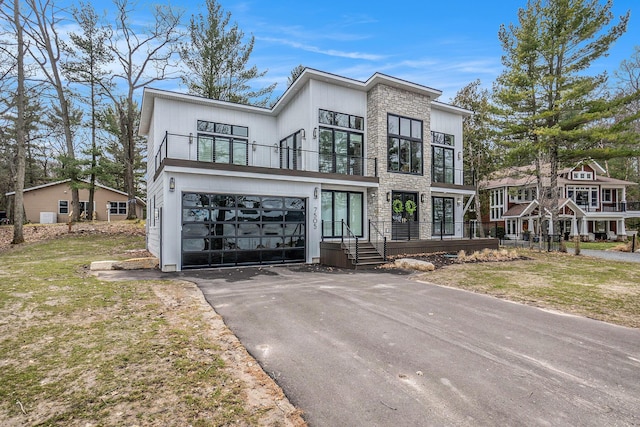 view of front of house with a garage, aphalt driveway, a balcony, and stone siding