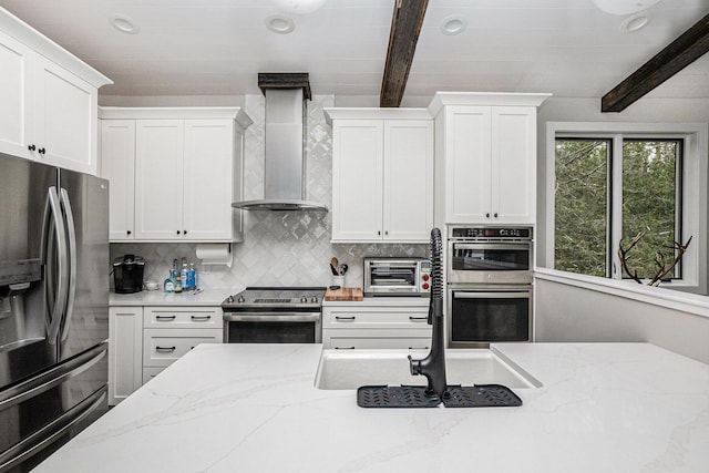 kitchen featuring tasteful backsplash, white cabinets, wall chimney range hood, beamed ceiling, and stainless steel appliances