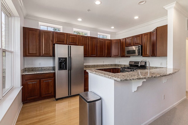 kitchen featuring light stone countertops, appliances with stainless steel finishes, a peninsula, light wood-type flooring, and a kitchen bar