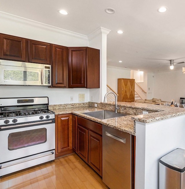 kitchen featuring ornamental molding, a peninsula, light wood-type flooring, a sink, and appliances with stainless steel finishes