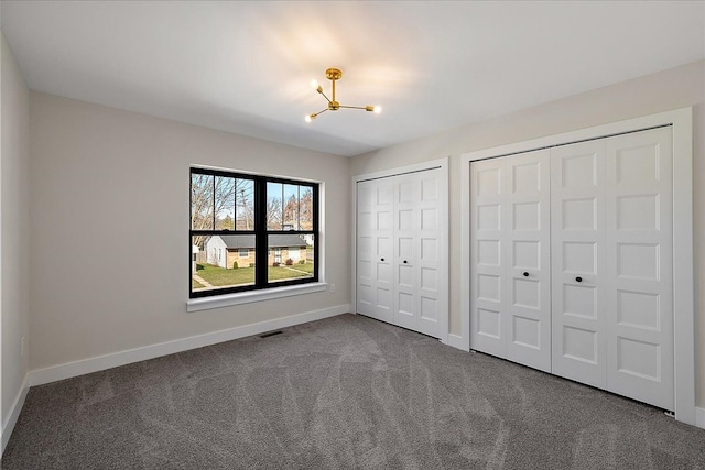 unfurnished bedroom featuring a chandelier, dark carpet, baseboards, and multiple closets