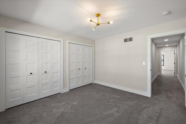 unfurnished bedroom featuring dark carpet, two closets, baseboards, and visible vents