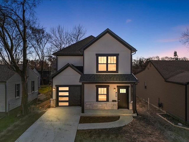 view of front facade featuring a shingled roof, stone siding, covered porch, stucco siding, and driveway