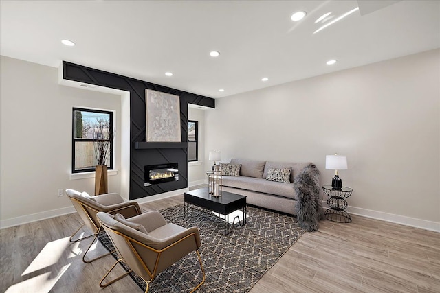 living area featuring a large fireplace, baseboards, recessed lighting, and light wood finished floors