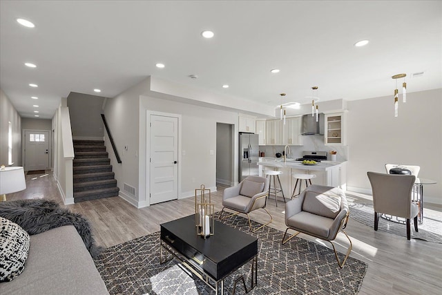 living room featuring visible vents, baseboards, recessed lighting, light wood finished floors, and stairway