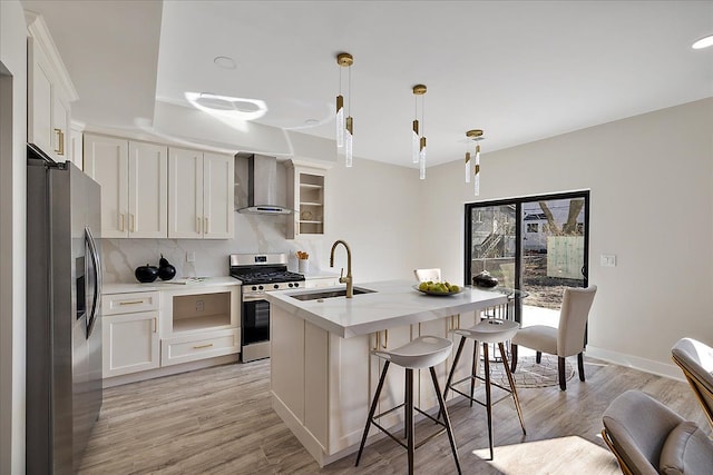 kitchen with tasteful backsplash, a sink, wall chimney range hood, an island with sink, and stainless steel appliances