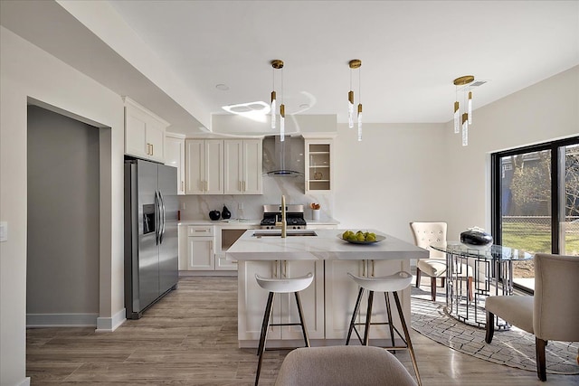 kitchen with a kitchen bar, tasteful backsplash, wall chimney range hood, light countertops, and stainless steel appliances