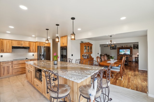 kitchen with a center island, under cabinet range hood, black appliances, recessed lighting, and light stone counters