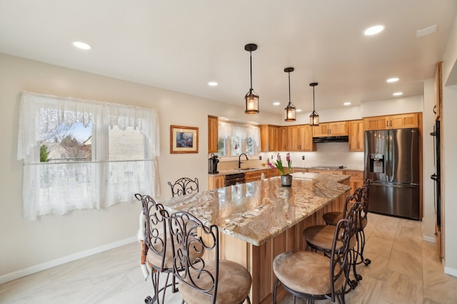 kitchen with a kitchen breakfast bar, black appliances, under cabinet range hood, light stone counters, and a sink