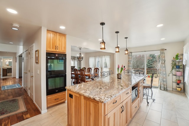 kitchen with dobule oven black, light stone countertops, a kitchen bar, a notable chandelier, and built in microwave