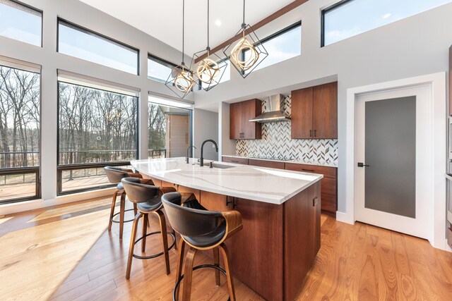 10485 Hadley Rd, Gregory, MI 48137 - kitchen with light wood-style floors, brown cabinetry, wall chimney range hood, a sink, and decorative backsplash
