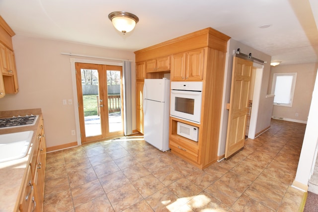kitchen with white appliances, french doors, light countertops, a barn door, and light brown cabinetry
