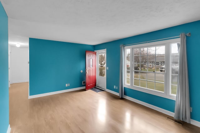 empty room with a textured ceiling, wood finished floors, baseboards, and visible vents