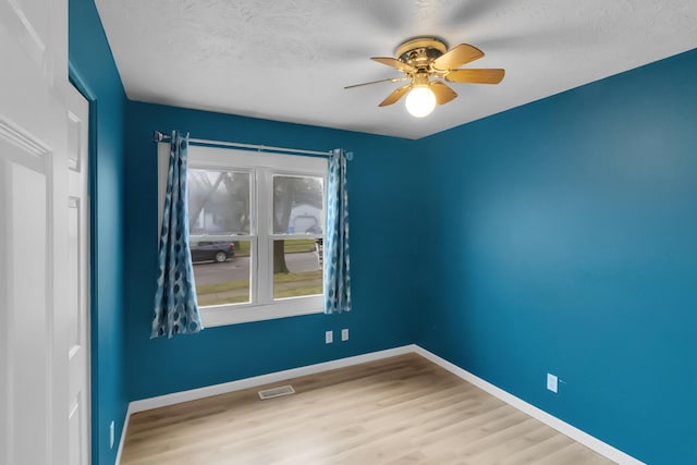spare room with a textured ceiling, a ceiling fan, visible vents, wood finished floors, and baseboards