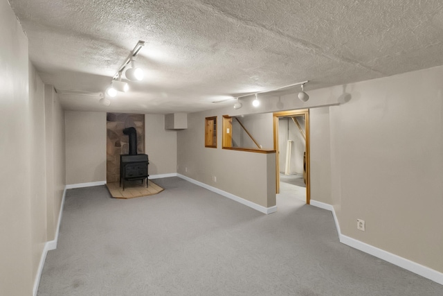 finished below grade area with a wood stove, a textured ceiling, baseboards, and carpet floors