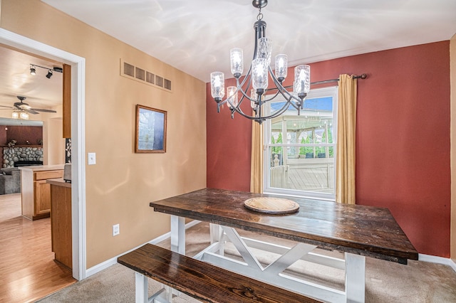 dining space with a chandelier, a stone fireplace, baseboards, and ceiling fan