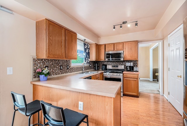 kitchen with stainless steel appliances, a sink, light countertops, a peninsula, and light wood finished floors