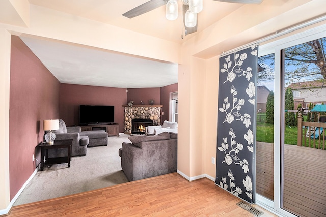 living area featuring wood finished floors, ceiling fan, a stone fireplace, and baseboards