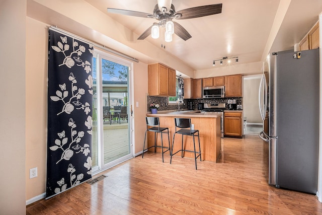 kitchen with stainless steel appliances, a peninsula, tasteful backsplash, light wood-style floors, and a sink