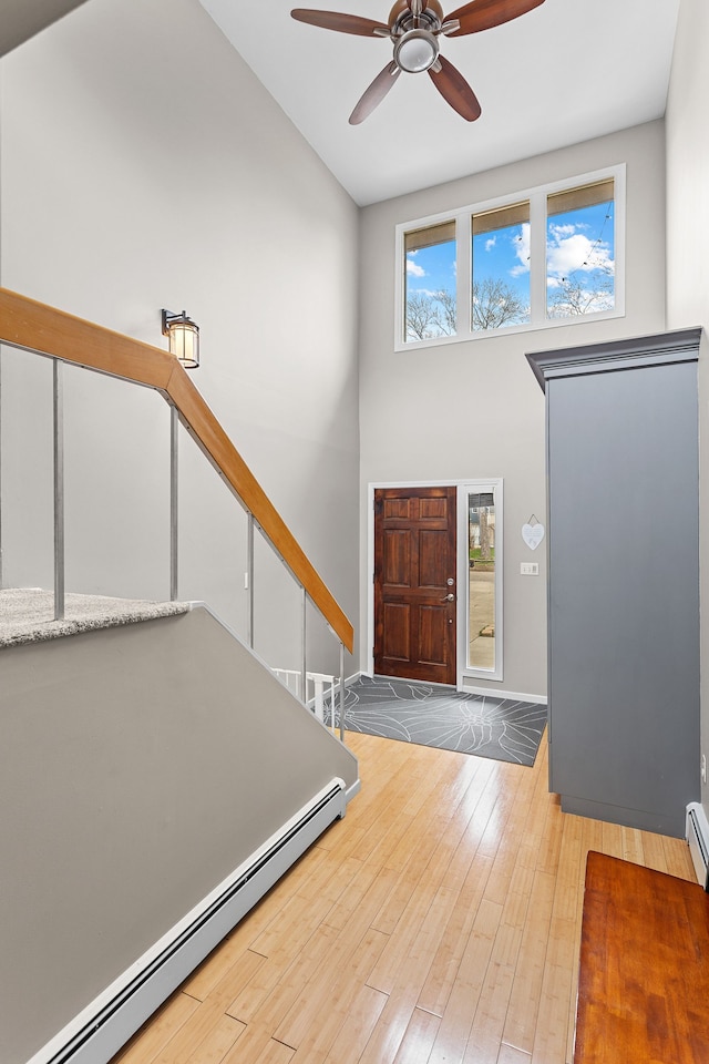 foyer entrance with baseboards, a high ceiling, a baseboard heating unit, a ceiling fan, and hardwood / wood-style floors
