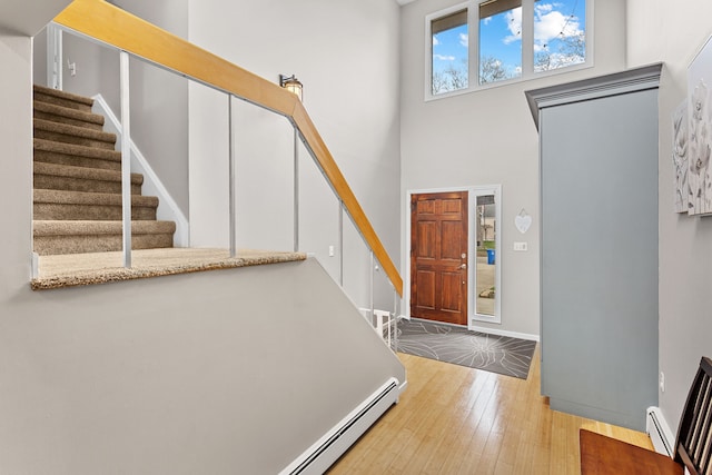 foyer with baseboard heating, a towering ceiling, wood-type flooring, and stairs