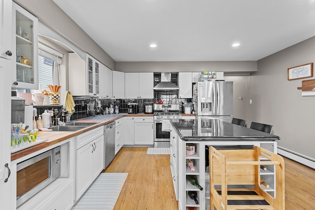 kitchen with a sink, appliances with stainless steel finishes, wall chimney exhaust hood, and light wood-style floors