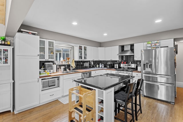 kitchen featuring light wood-type flooring, wall chimney range hood, white cabinetry, and stainless steel appliances