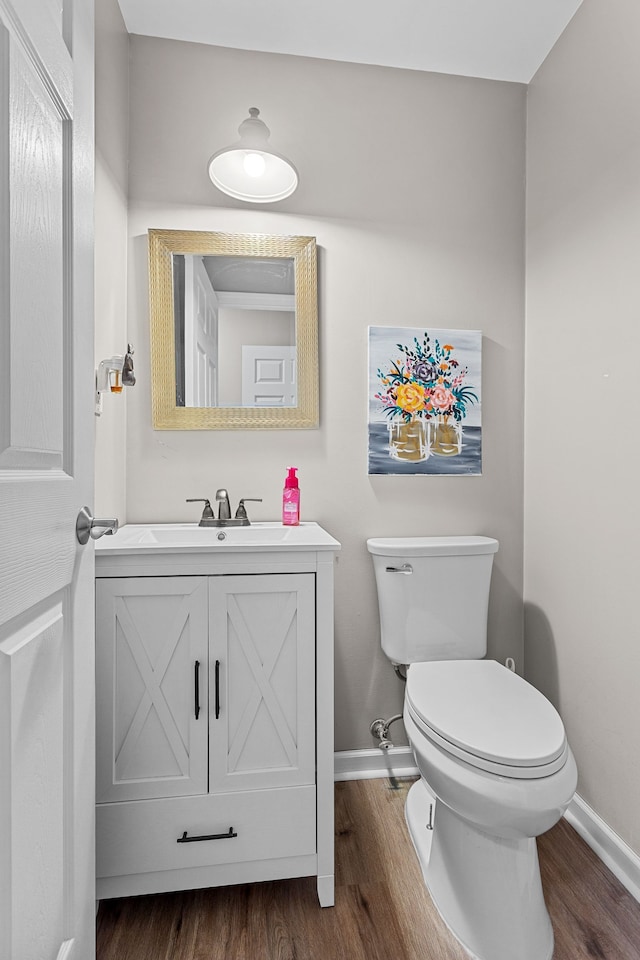 half bathroom with vanity, baseboards, toilet, and wood finished floors