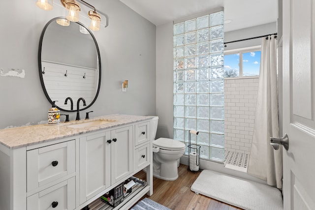 bathroom featuring vanity, a tile shower, toilet, and wood finished floors