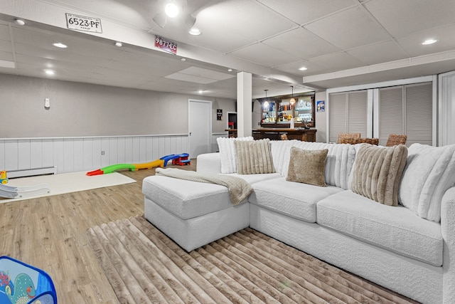 living area with baseboard heating, a paneled ceiling, a wainscoted wall, wood finished floors, and bar