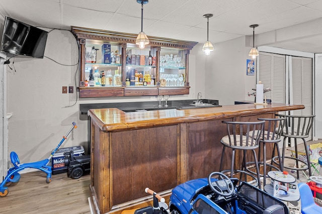 bar featuring light wood-style floors, wet bar, pendant lighting, and a drop ceiling