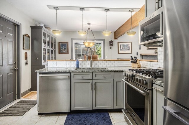 kitchen with tasteful backsplash, a peninsula, gray cabinetry, stainless steel appliances, and a sink